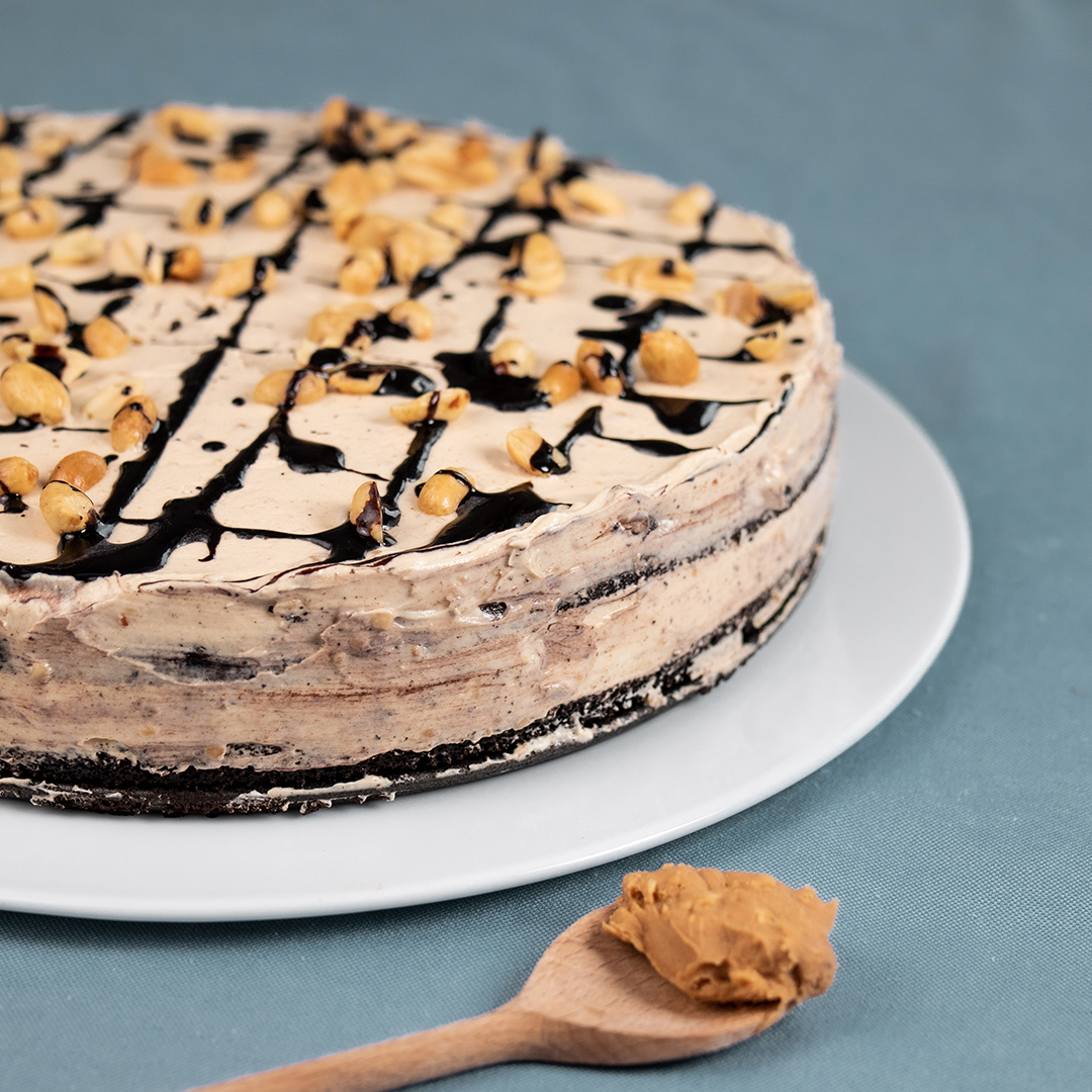 Vegane Erdnuss-Schoko-Torte auf blauem Tischtuch mit Holzlöffel mit Peanutbutter daneben