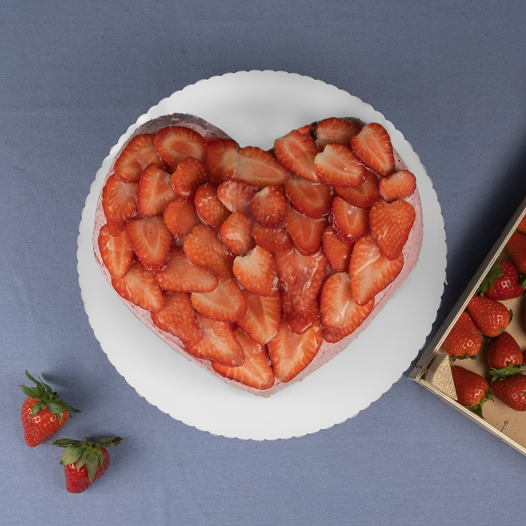 Herzförmige Torte mit Vanilleboden, Erdbeersahne und frischen Erdbeeren auf einem weißen Teller