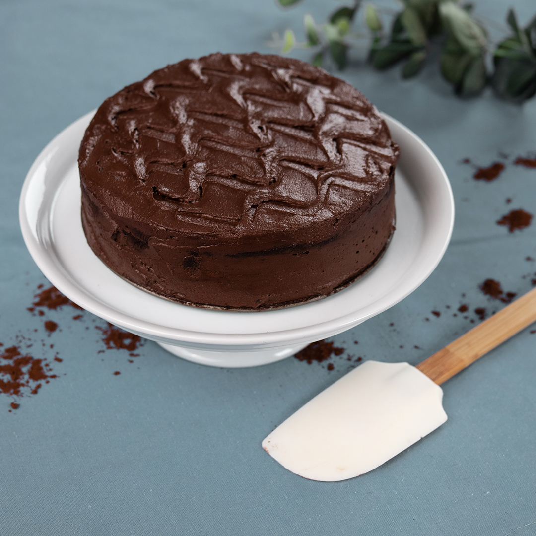 Vegane Death by Chocolate-Torte auf weißem Teller, daneben weißer Spatel auf blauem Tischtuch